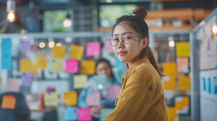 A focused corporate Asian woman leading a team brainstorming session in a vibrant collaborative workspace, surrounded by colorful whiteboards and post-it notes.