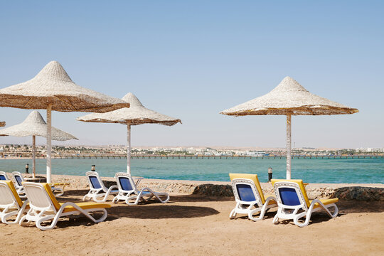 row of white sun loungers under straw umbrellas