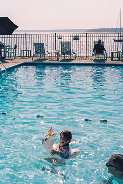 Child Swims in an Outdoor Pool with a Floatie, her Dad at her Side