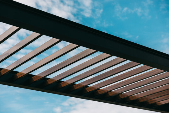 Modern wooden pergola against a blue sky with clouds