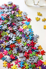 Colorful jigsaw puzzle pieces, cup of tea or coffee, eyeglasses and fresh berries for snacking. Hygge at home. Selective focus.