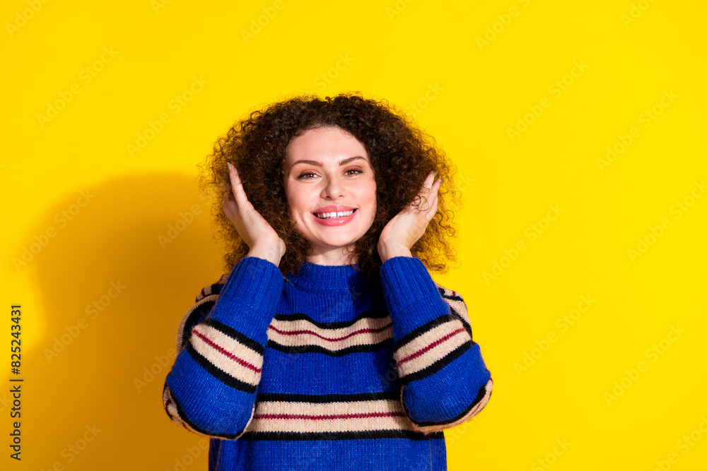 Wall mural Portrait of adorable cheerful girl with wavy hairstyle wear knit pullover hands hold curly hairdo isolated on yellow color background