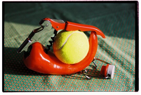 Conceptual still life with red pepper, an opener and a tennis ball.