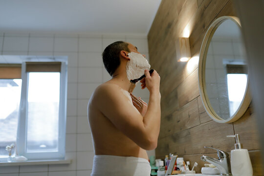 a young man shaves with a razor in the bath
