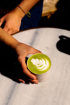 A person is holding a cup of a specialty matcha latte