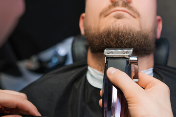 Master skillfully trims the clients beard using an automatic trimmer in the barbershop