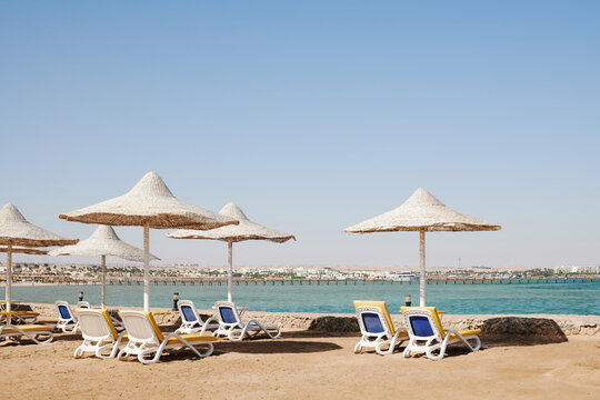 row of white sun loungers under straw umbrellas