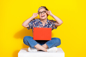 Full size photo of nice pensioner female sit cube netbook laugh wear trendy colorful outfit isolated on yellow color background