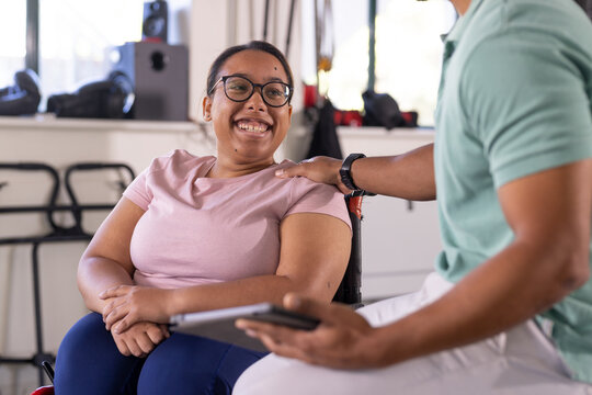 A biracial female paraplegic patient smiling at gym rehab center with therapist