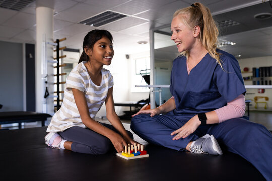 At rehabilitation center, Caucasian female physical therapist aids biracial girl with cerebral palsy