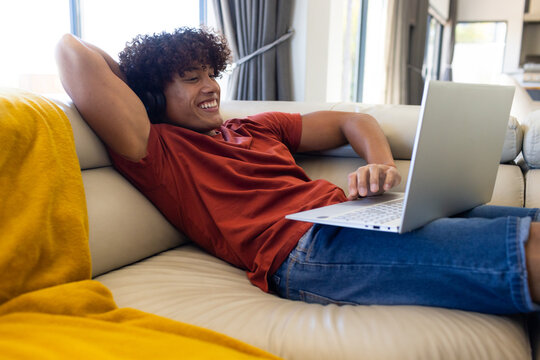 A biracial young male wearing headphones, using laptop at home