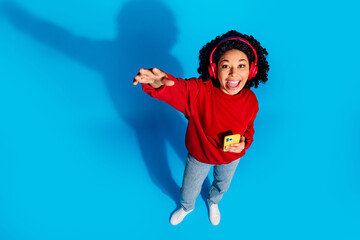 Full length photo of lovely young lady top view stretch arm headphones device dressed stylish red garment isolated on blue color background