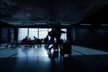People at an airport terminal, walking with luggage and sitting, waiting for their departure time,...