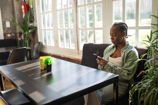 black woman using mobile phone sitting in a cafe