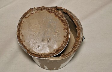 Rusted old metal paint tin with open lid on drop cloth brown expired storage concept.