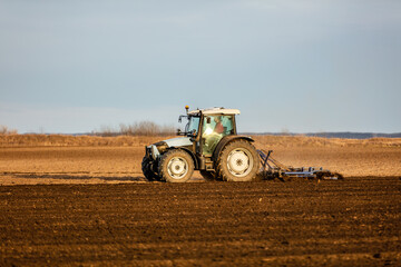 Fototapeta premium Tractor with a plow attachment tilling the soil in a vast farmland setting