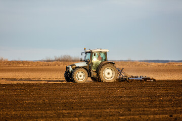 Tractor with a plow attachment tilling the soil in a vast farmland setting