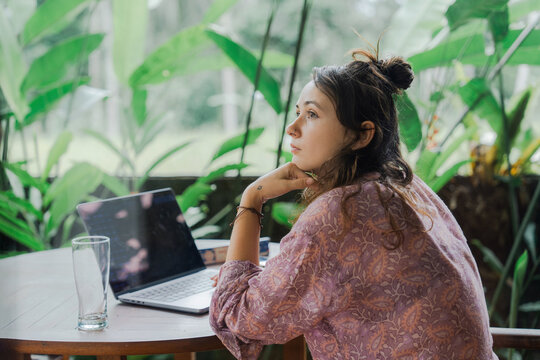 Woman in thoughts sitting at the table with laptop in front of her