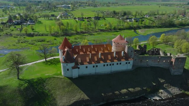Aerial establishing view of Bauska Medieval Castle and ruins, Musa and Memele rivers next to the castle, sunny spring day, wide drone shot moving forward, camera tilt down