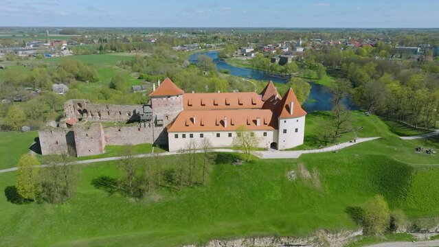 Aerial establishing view of Bauska Medieval Castle and ruins, Musa and Memele rivers next to the castle, sunny spring day, distant wide orbiting drone shot