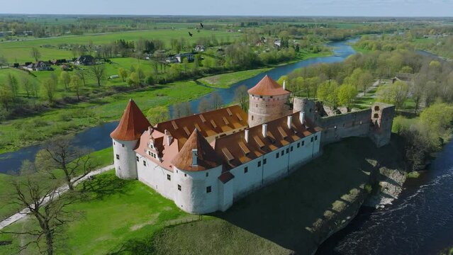 Aerial establishing view of Bauska Medieval Castle and ruins, Musa and Memele rivers next to the castle, sunny spring day, wide orbiting drone shot