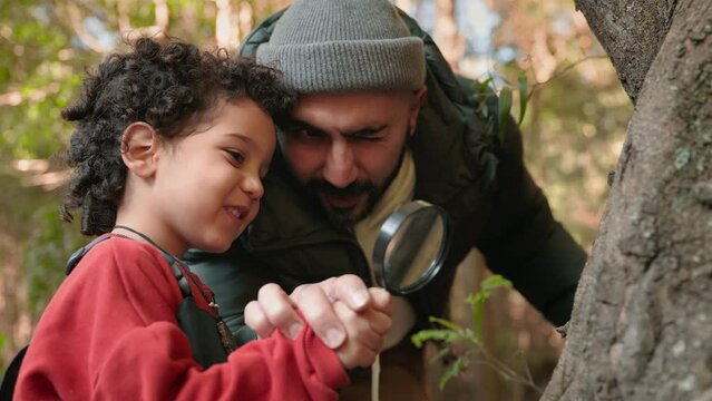 A joyful moment as a father and son inspect nature closely with a magnifying glass in a forest setting, expressing curiosity and bonding.