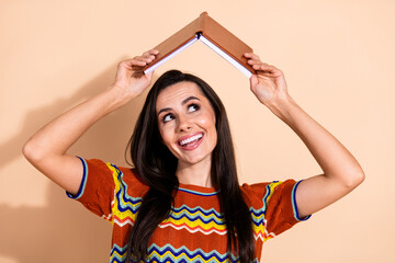 Photo of nice young woman book above head look empty space wear t-shirt isolated on beige color...
