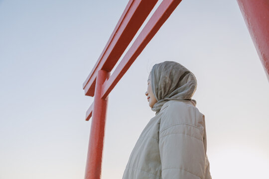 A woman praying in front of a torii gate on the seashore.