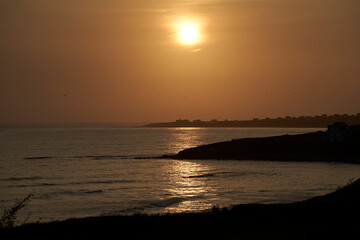Fototapeta premium Sunset over the coast in France. Village silhouette by the sea in Brittany. Landscape ideal as background for postcard.