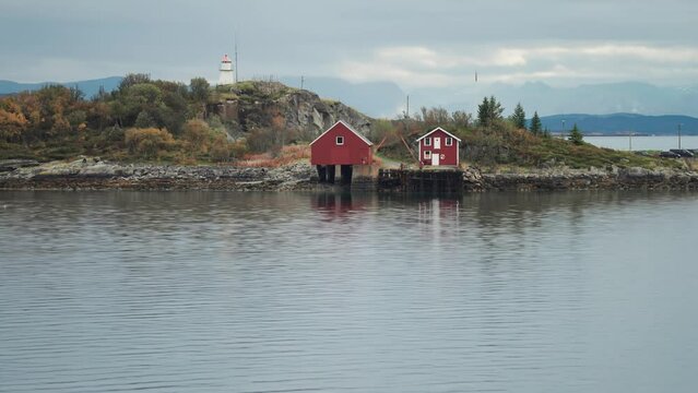 Tidy cottage, boathouse, and a small lighthouse on the small island on the rocky coast of Lofoten.