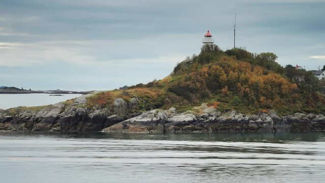 A miniature lighthouse on the small grass-covered rocky island. Coastal village in the background.