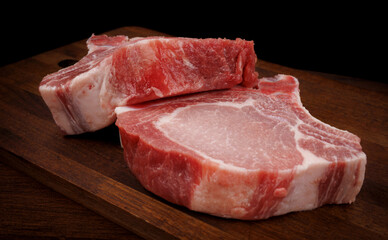 Two pork entrecotes lie on a wooden cutting board. Pork .