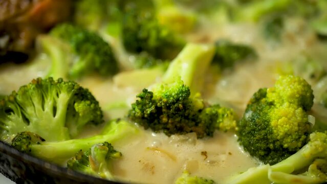 Fry green colorful broccoli in creamy sauce over low heat in a frying pan close-up. The simmering sauce bubbles with juicy, vibrant broccoli. Vegetable roast. Vegetarian food