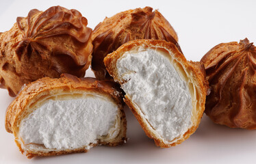 Cut in half and whole porophytroles with white cream on a white background. Eclair with cream.