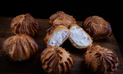 Profiteroles with white custard on a wooden board. Mini eclairs with white cream.