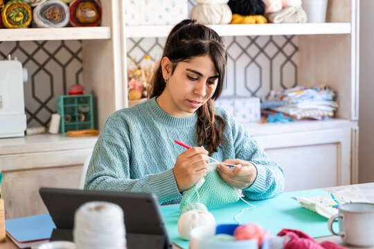Woman engaged in knitting while looking at tablet