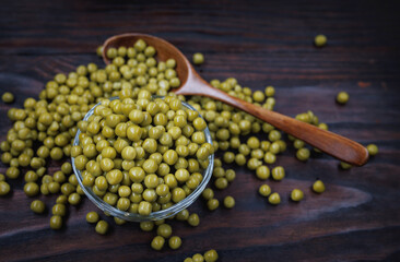 Canned green peas in a wooden spoon lying on a wooden surface of the table.