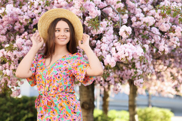 Beautiful woman in straw hat near blossoming tree on spring day