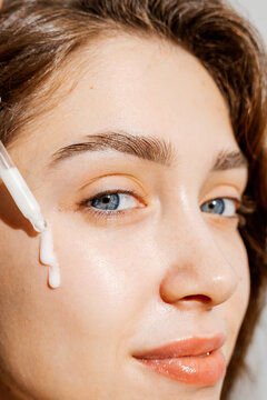 Skincare Portrait. A young woman applies facial oil to radiant skin