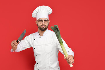 Professional chef with leek and knife having fun on red background. Space for text