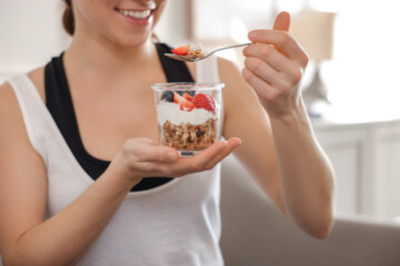 Woman eating tasty granola with fresh berries and yogurt at home, closeup