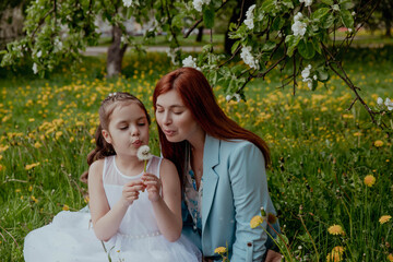 Obraz premium Mother and daughter in blooming garden blowing dandelions