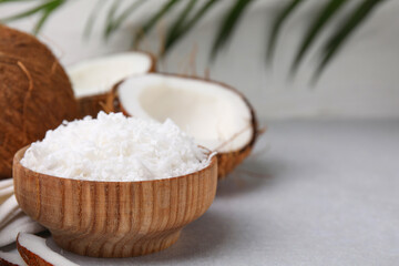 Coconut flakes in bowl and nuts on light grey table, space for text