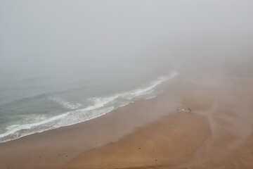Foggy beach with waves and walkers