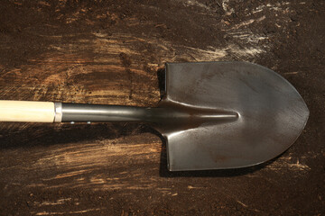 Metal shovel with fertile soil on dirty wooden surface, top view
