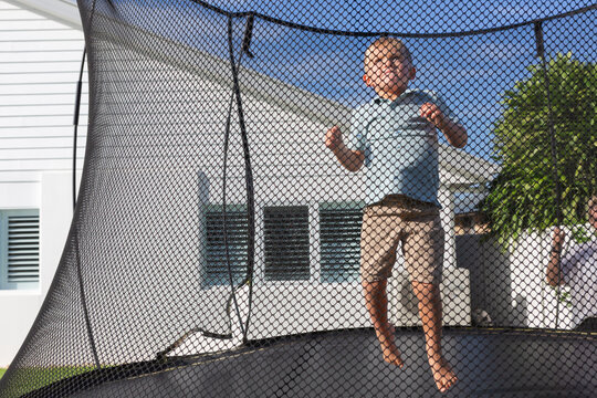 Boy happily bouncing on a trampoline with net