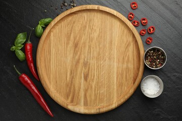Cutting board, salt, spices, basil and chili peppers on black textured table, flat lay. Space for...