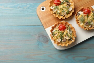 Tasty tartlets with cheese, tomatoes, mushrooms and dill on turquoise wooden table, top view. Space for text