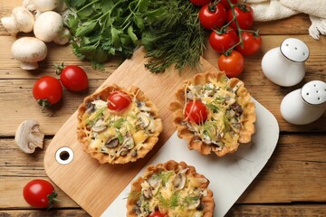Tasty tartlets with cheese, tomatoes, mushrooms and dill on wooden table, flat lay