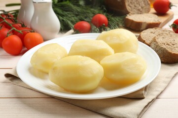 Plate with young boiled potatoes on light wooden table, closeup